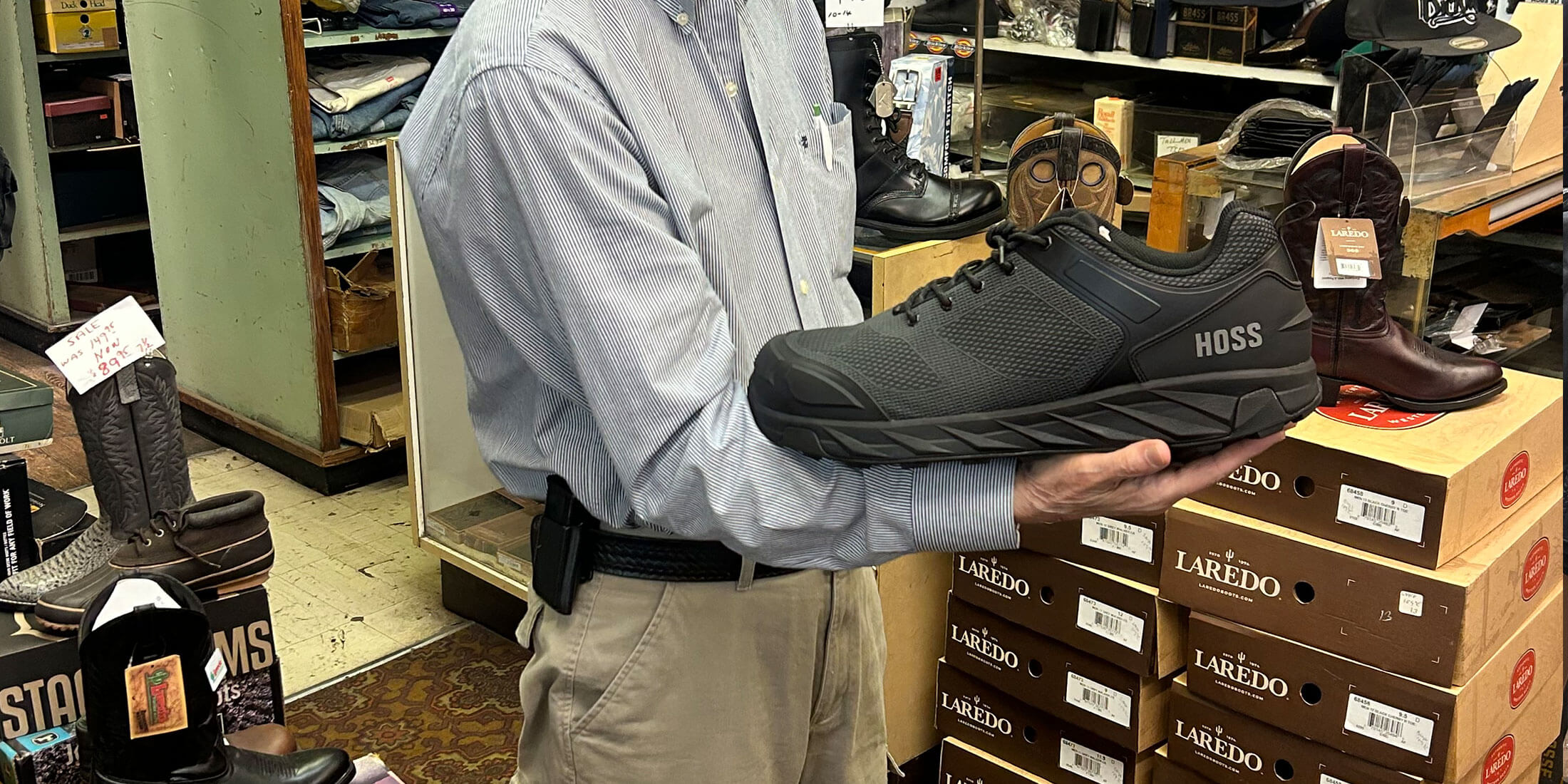 A black HOSS work shoe held up beside stacks of Laredo boot boxes and western boots at Kornfeld's.